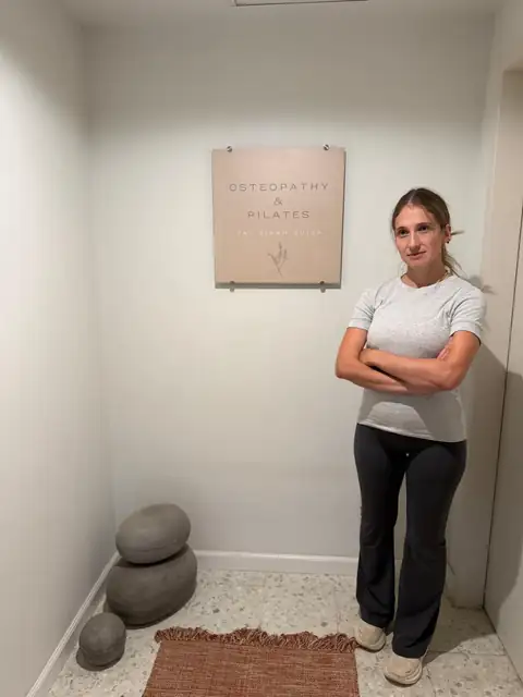 טל בירם סויסה עומדת בסטודיו ליד שלט אוסטאופתיה ופילאטיס
