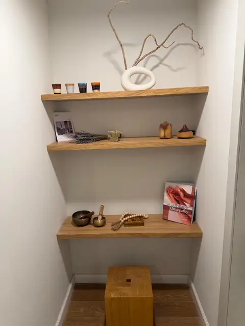מדפי עץ בסטודיו עם קערות טיבטיות, לבנדר וספר אוסטאופתיה לילדים
